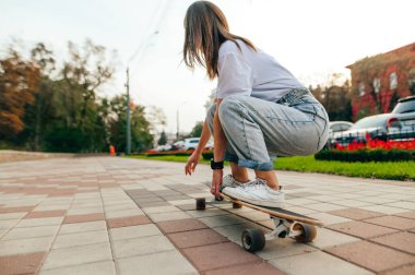 Gündelik giysiler içinde şık bir kadın, uzun bir tahtanın üzerinde hızla caddede yürüyor. Arka tarafta oturuyor. Kadın kaykaycı, sokağın aşağısında oturan bir kaykayın üzerinde hareket ediyor.