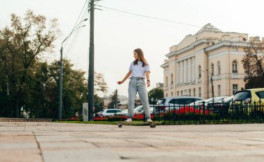 Şık giyinmiş kadın kaykaycı şehrin sokaklarında sörf tahtasına biniyor. Paten konsepti. Tahtada yürü.