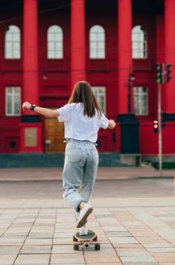 Şık bir kadın şehrin sokaklarında uzun bir tahtanın üzerinde dikiz aynasıyla yürüyor. Kadın kaykaycı bir sapan kullanıyor. Arkadan bak. Dikey.