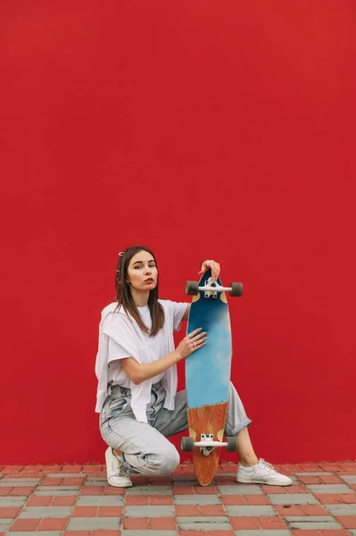 Mulher Elegante Roupas Casuais Senta Com Skate Mão Fundo Vermelho — Fotografia de Stock