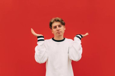 Ciddi bir suratı olan kafası karışmış bir adam kırmızı bir duvara karşı duruyor ve kafası karışmış bir şekilde kameraya bakıyor. İzole edilmiş.