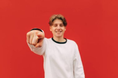 Mutlu adam kırmızı arka planda kameraya parmağını gösterir ve gülümser. Parmaklarına odaklan. İzole edilmiş