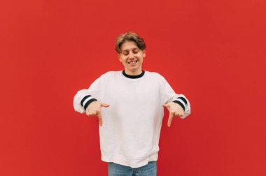 Kırmızı duvarda dikilen sıradan elbiseli mutlu genç adam yüzünde gülümsemeyle fotokopi alanında parmaklarını gösteriyor.