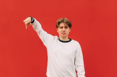 Pozitif genç adam fotokopi alanının kenarını işaret ediyor ve kırmızı duvara karşı izole edilmiş şaşkın buzla kameraya bakıyor..