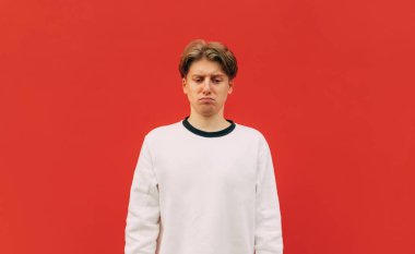 Kırmızı duvarda parlak elbiseli üzgün bir gencin portresi, başı eğik ve üzgün. İzole edilmiş üzgün bir adamın portresi..