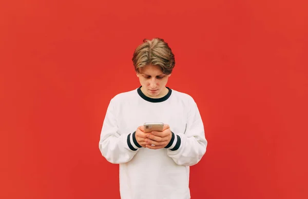 Skoncentrowany Młody Człowiek Białych Ubraniach Casual Korzysta Smartfona Ulicy Tle — Zdjęcie stockowe