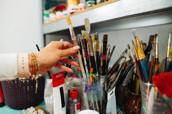 妇女的手从架子上拿起画笔作为绘画工具 女人的手和画笔图片制作过程中的图片 — 图库照片