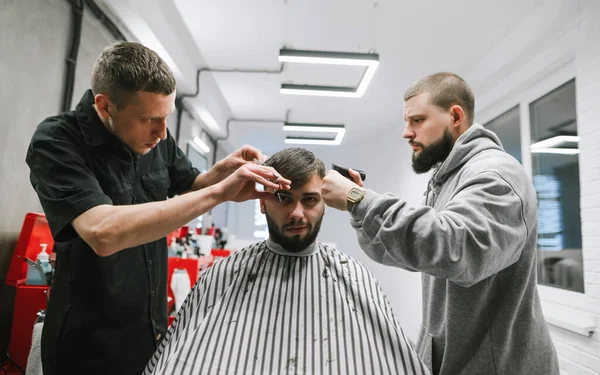 スタイリッシュな軽床屋で髭の男の髪を切る2つの理髪店 2人の美容師が依頼人を切りました 男性用ヘアカットのワークショップ 理容室のマスタークラス — ストック写真