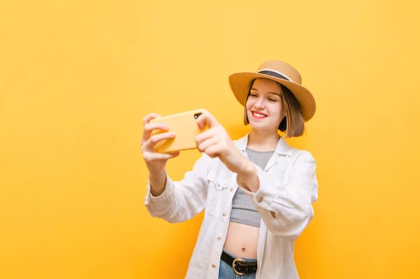 明るい夏の服の笑顔の女性は スマートフォンでモバイルゲームをプレイし 彼女の顔に笑顔で画面を見て 黄色に隔離された 彼女の電話でオンラインゲームをプレイし 笑みを浮かべて陽気な女性 — ストック写真