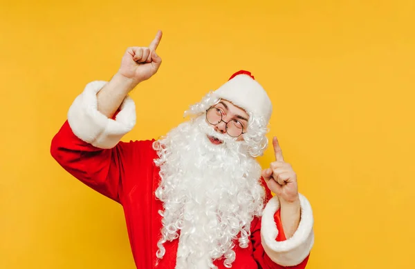 圣诞快乐 圣诞老人正在促销 把他的手指指向一个复制的空间 圣诞老人站在演播室的黄色背景上 向观众展示一些东西 — 图库照片
