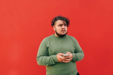 Kendine güvenen genç şişman adam, akıllı telefonundan müzik dinlemek için kablosuz kulaklık kullanıyor, seslere konsantre oluyor..