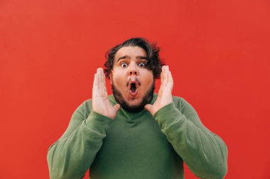 Komik, yakışıklı İspanyol adam şakayla izleyicilere bağırıyor, dikkat çekiyor, bağırıyor, kırmızı arka planda duruyor..