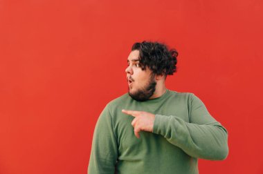 Fotokopi çekilen yeri işaret eden şaşkın, genç, şişman bir İspanyol 'un yan görüntüsü, kırmızı bir arka plan, ağzını şaşkınlıkla açıyor..