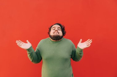 Kafası karışmış ve komik, şişman, İspanyol bir adam bir jestle kafasını karıştırıyor ellerini kaldırıp kırmızı bir duvarın önünde duruyor..