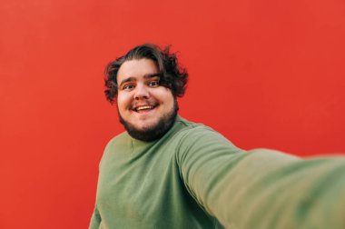 Gülümseyen mutlu genç adam, bir kamerada özçekim fotoğrafı çekiyor, son derece neşeli, dişlek bir gülümseme gösteriyor, kameraya bakıyor..