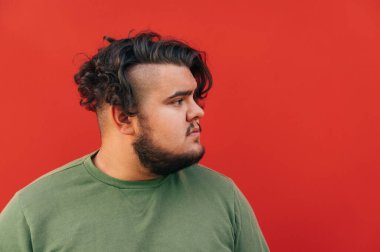 Yakışıklı, sakallı, Latin kökenli genç bir adam, ciddi görünüyor, kırmızı arka planda bir fotoğraf için poz veriyor. Yakın plan portre.