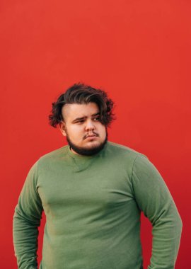 Şişman, sakallı, stil sahibi, kıvırcık saçlı, kırmızı duvarın önünde dikilmiş, ciddi ciddi yana bakan bir İspanyol 'un dikey portresi..