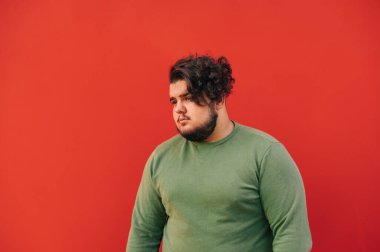 Şişman sakallı İspanyol bir adamın portresi. Şık bir saç kesimi ve kıvırcık saçı var. Kırmızı duvarın önünde duruyor..