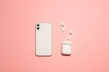 Beyaz bir akıllı telefon, kablosuz kulaklıklar ve izole edilmiş pembe arka planda şarj çantası olan minimal yerleşim fotoğrafı..