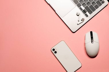 Gümüş gri dizüstü bilgisayarı, modern akıllı telefonu, beyaz plastik faresi ve pastel pembe arka planda kablosuz kulaklığı olan minimal düz bir fotoğraf..