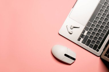 Minimum düz dizüstü bilgisayar, siyah klavye, kablosuz kulaklık ve pembe arka planda beyaz bir bilgisayar faresi..