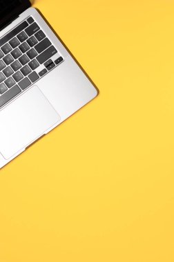 Sarı bir zemin üzerinde, siyah klavyeli, modern gri bir dizüstü bilgisayarla yatar vaziyette duran minimalist düz bir fotoğraf..