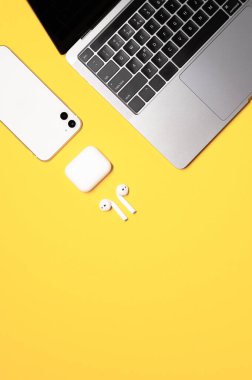 Gümüş gri dizüstü bilgisayar, beyaz akıllı telefon, sarı arka planda şarj çantası olan kulaklıklar..