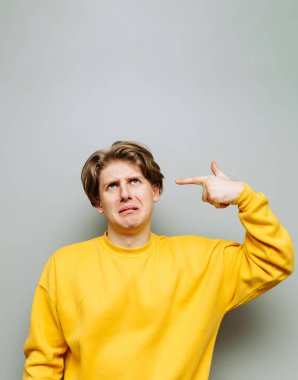 Sarı elbiseli sefil bir adam gri bir duvarın arkasında duruyor ve parmağıyla kafasına silah dayayıp ağlıyor..