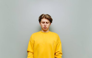 Gri arka planda sarı elbiseli üzgün bir adamın portresi, aşağılanmış görünüyor. Üzgün genç adam, gri duvar arka planında izole..