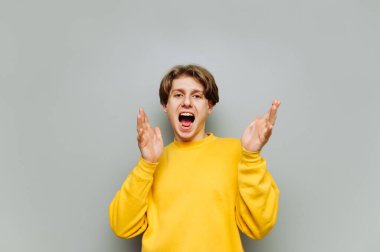 Neşeli bir adam gri bir duvarın arka planında duruyor, ağzı açık ve mutlu bir yüzle kameraya bakıyor, sarı kıyafetler giyiyor, izole edilmiş..