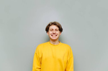 Gri arka planda sarı kazaklı bir adamın portresi yüzünde bir gülümsemeyle kameraya bakar ve dişlerini gösterir. İzole edilmiş.