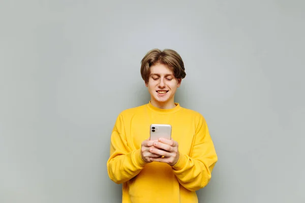 Jovem Feliz Roupas Amarelas Usa Smartphone Fundo Cinza Com Sorriso — Fotografia de Stock