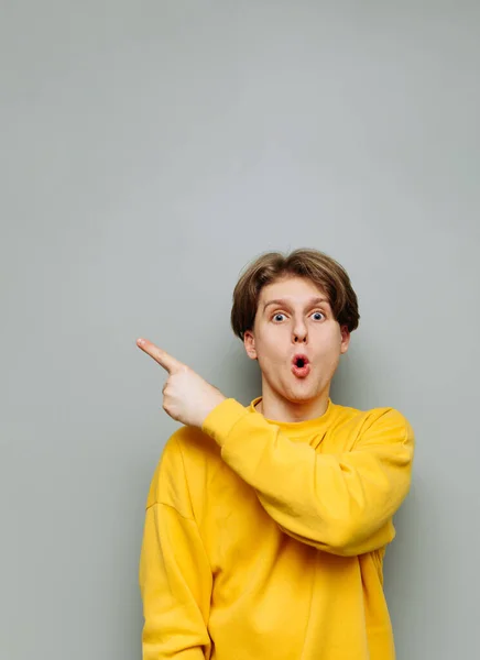 Шокированный Молодой Человек Желтой Одежде Стоит Фоне Серой Стены Показывает — стоковое фото