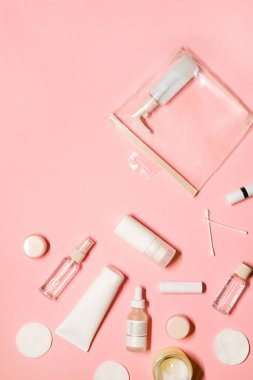 Cilt bakımı ürünleri ile dikey düz çekim: şampuan, deodorant, krem, yüz sisi, esans, serum, ruj, merhem, pamuk pedleri ve pastel pembe arka planda bir mum..