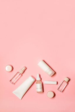 Cilt kremi, deodorant, ruj, serum, gerekli yağ, dudak kremi ve yüz maskesi gibi pembe arka planda bir fotokopi alanı ile dikey düz çekim..