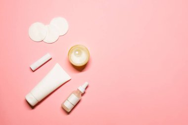 Kozmetik ürünleri olan basit düz yatak fotoğrafı: nemlendirici, krem, serum, ruj, pamuk pedler ve pembe arka planda bir mum. Boşluğu sağ tarafa kopyala.