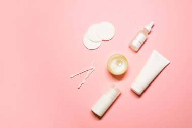Düz cilt bakımı ürünleri: pamuk pedler ve tomurcuklar, yüz kremi, serum, deodorant ve pembe arka planda bir mum..