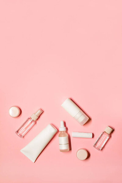 Вертикальный плоский снимок с копией пространства на розовом фоне с товарами по уходу за кожей: кремом для рук, дезодорантом, помадой, сывороткой, эфирным маслом, бальзамом для губ и маской для лица.
