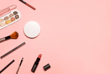 Makyaj malzemeleriyle birlikte pastel pembe arka plan üzerine şık bir düz çekim: renkli göz farı, fırçalar, gül ruju, göz kalemi, göz ve dudak kalemi ve pamuk pedler.