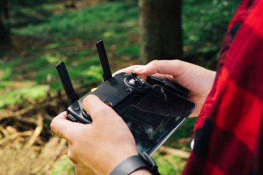 Uzaktan kumandalı bir pilotun elleri İHA 'yı kontrol etmek için Ormanda uçan bir erkek turist, Uzaktan kumandalı eller, yakın çekim