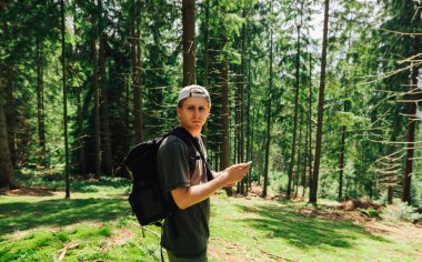 Yürüyüşünde sırtında sırt çantası, dağ kozalaklı bir ormanın ortasında elinde akıllı bir telefonla yürüyüşte dinlenen bir yürüyüşçü..