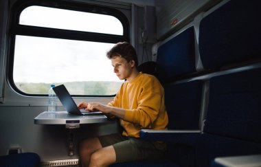 Masadaki trende çalışan konsantre olmuş serbest çalışan bir erkek. Adam trende dizüstü bilgisayar kullanıyor..