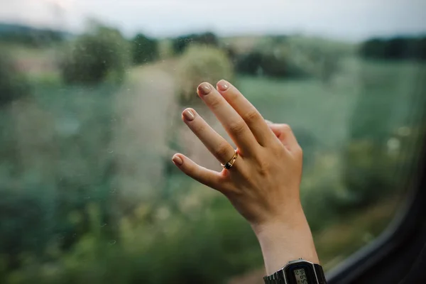 Woman's hand touches the train window on the road. Dreamy woman touches the window on the background of a beautiful view from the train.