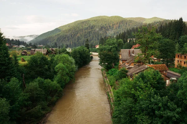 Mountain landscape with river and houses on the shore. Town in the mountains landscape, photo from the bridge. Vorokhta, Carpathians, Ukraine.