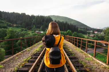 Sırtında sırt çantası olan bir kadın turistin arkası demiryolu köprüsünün üzerinde duruyor ve önüne bakıyor. Karpatlar ve Ukrayna 'da turizm.