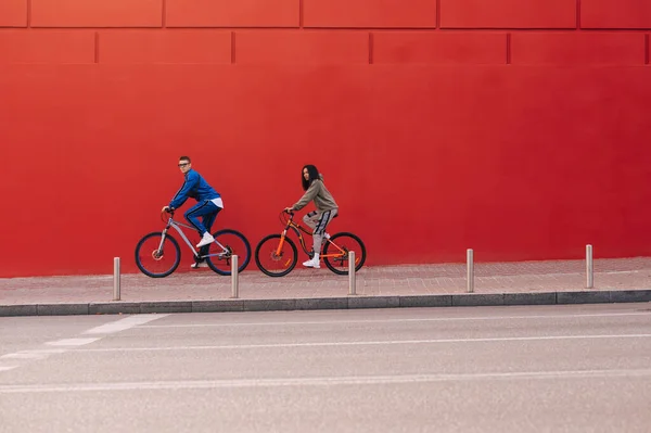 时尚的年轻人骑自行车在红墙的背景下走在城市街道上 一对运动型的自行车手骑在红色的背景上 — 图库照片