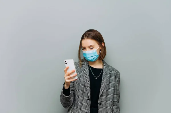 Attractive Woman Gray Suit Medical Mask Her Face Uses Smartphone — Stock Photo, Image