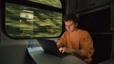 Yoğunlaşmış genç adam yoldaki bir trende dizüstü bilgisayar kullanıyor. Trenle seyahat ederken dizüstü bilgisayarda çalışan serbest çalışan biri..
