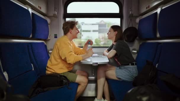 美しい若いカップルは 道路のテーブルで電車の中に座って 彼の顔に笑顔で通信します トラベルスビー列車のカップル — ストック動画