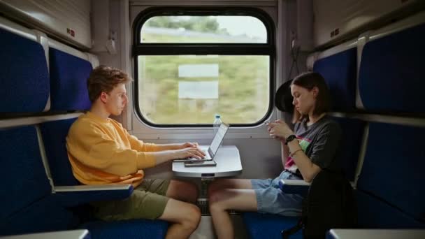 若い男と女がコンパートメントで電車に乗り ガジェットを使用し 男はノートパソコンで働き スマートフォンを持つ女の子 電車で旅をしてインターネットを楽しみ — ストック動画